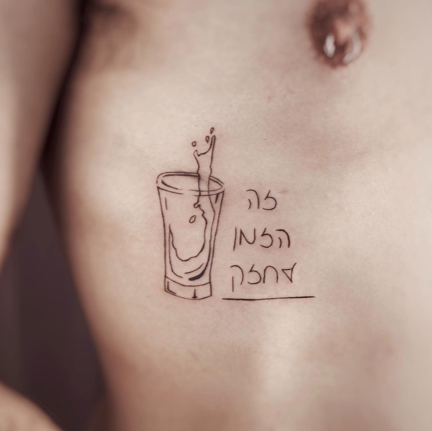 Tattoo on chest featuring a glass of spilled liquid with text in Hebrew
