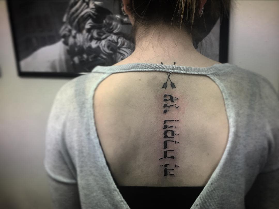 A woman with a back tattoo of Hebrew letters and arrow