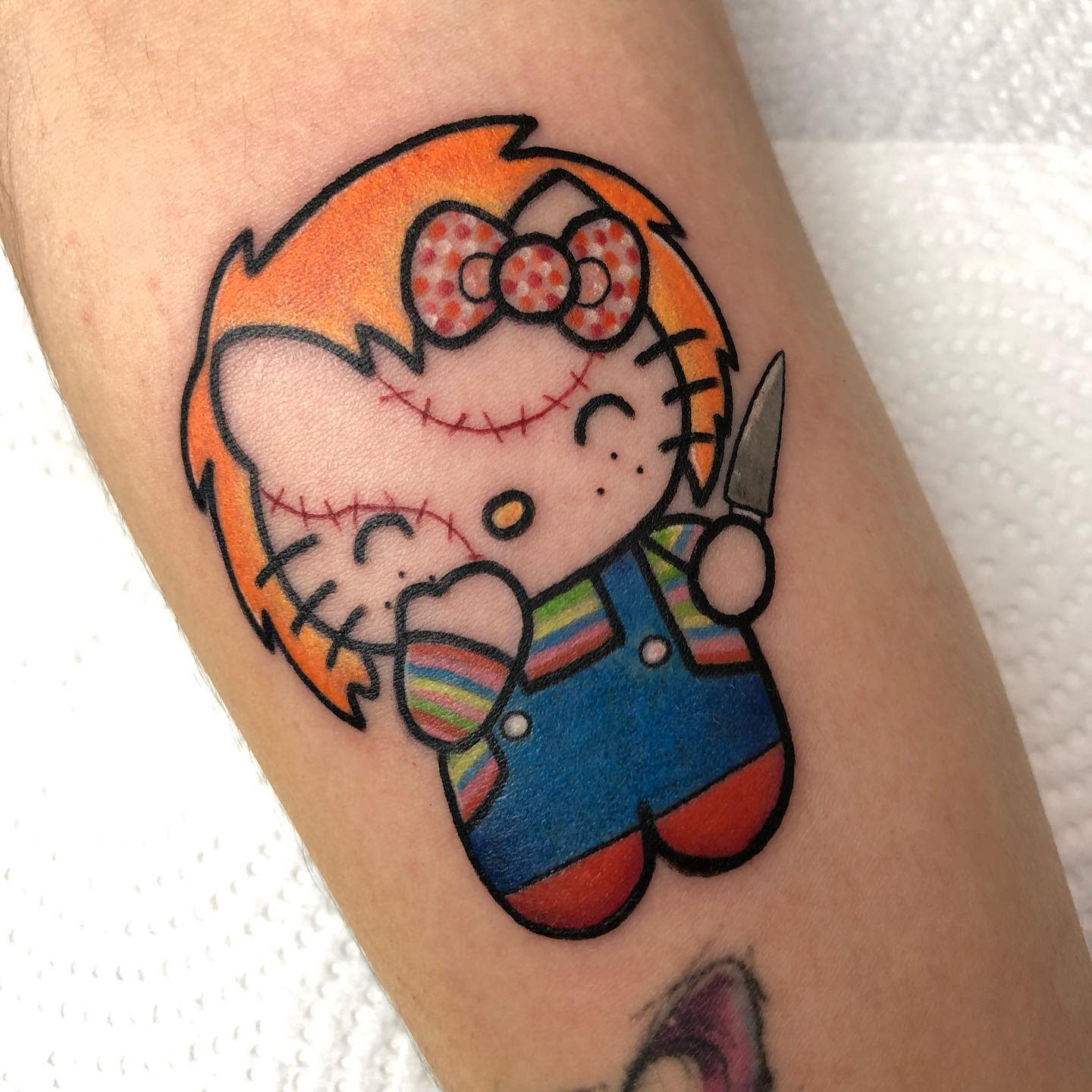 Tattoo of Hello Kitty dressed as Chucky, holding a knife, with stitched scars on the face