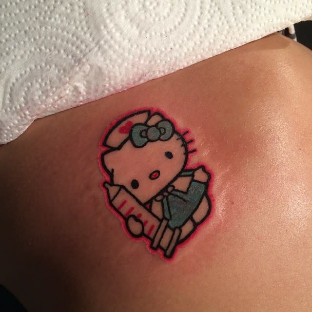 A Hello Kitty character dressed as a nurse holding a syringe tattoo against the skin