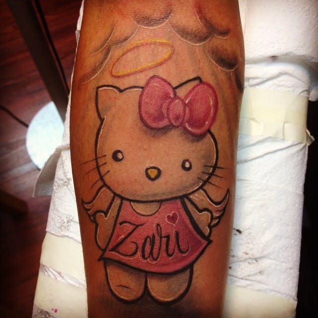Tattoo of Hello Kitty with a halo and wings, wearing a dress with "Zari" written on it