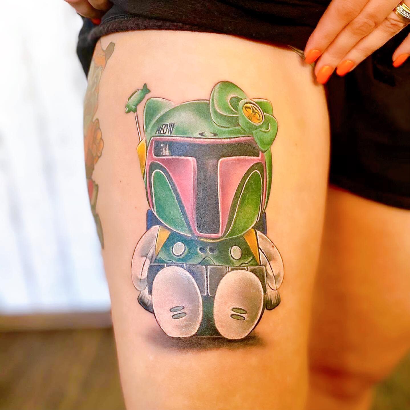 Tattoo of a cute character on a thigh blending Boba Fett helmet with Hello Kitty details
