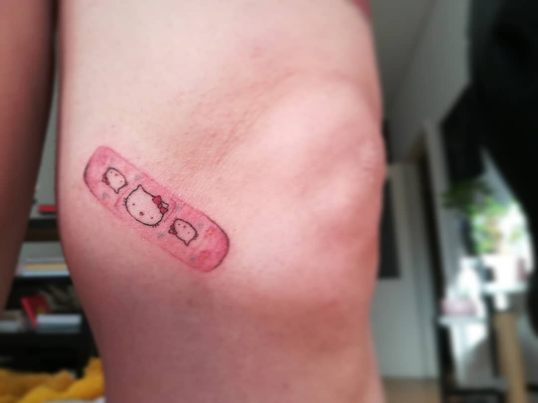 Tattoo of a pink Hello Kitty bandage on the back of a knee