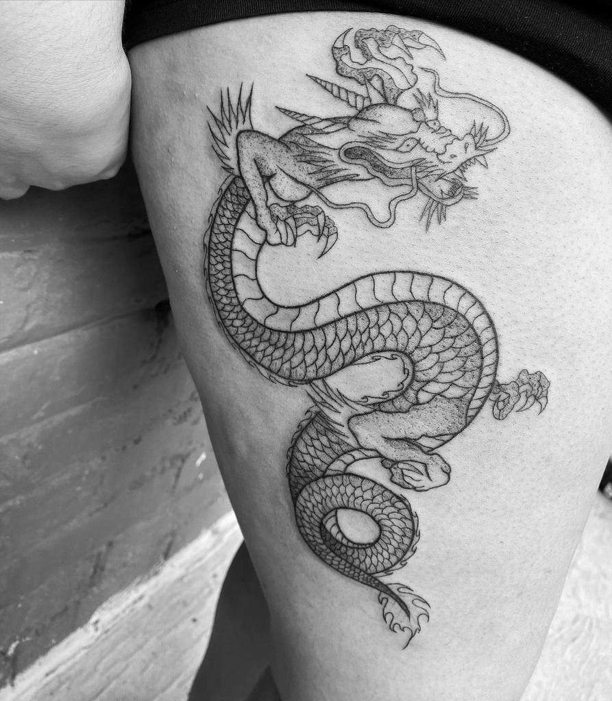 Black and white dragon tattoo on a woman's thigh