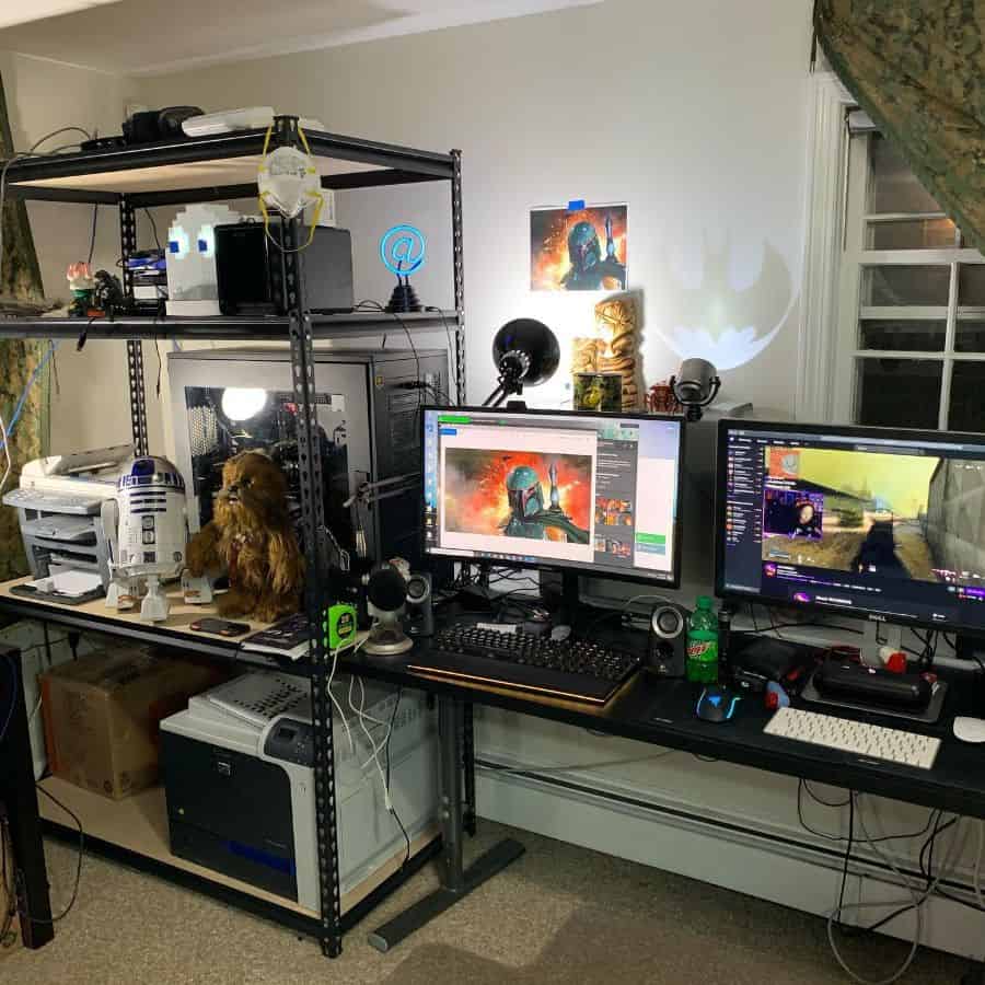 A gaming setup with dual monitors, shelves with Star Wars figures, and a printer in a brightly lit room