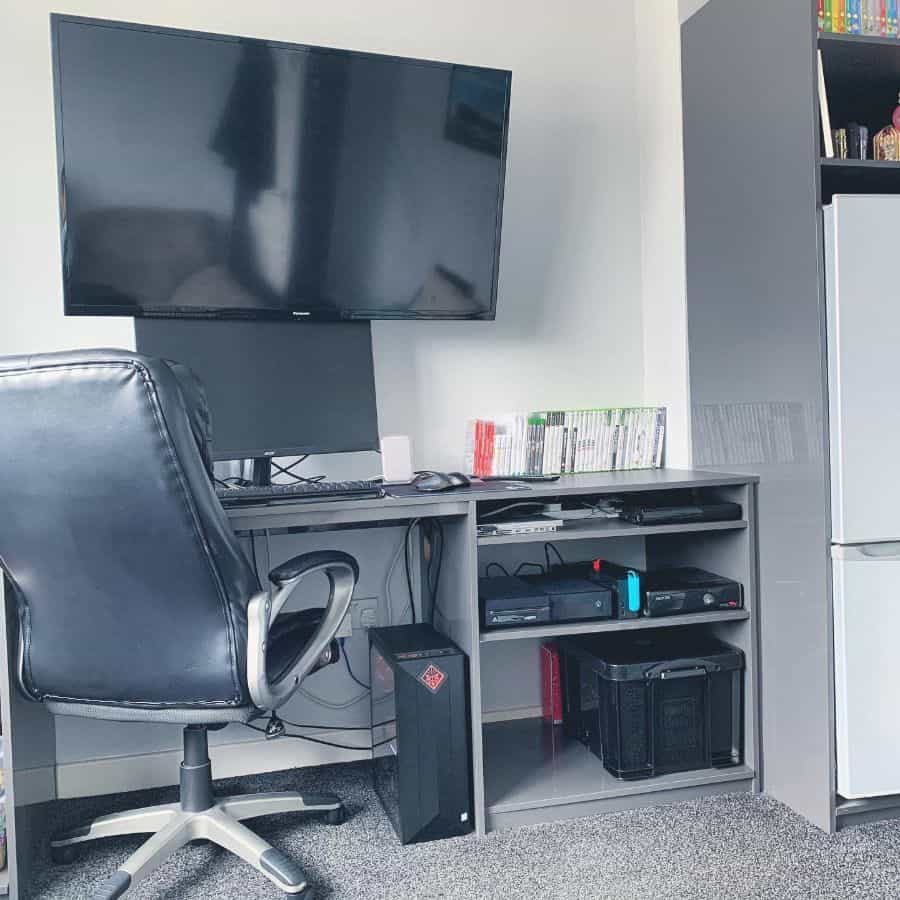 Home office with a desk, swivel chair, dual monitors, gaming console, and various games on shelves