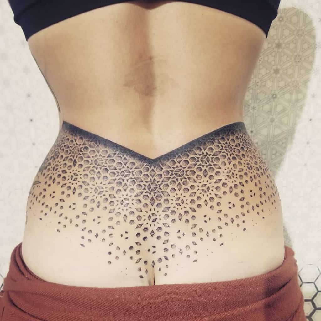 Lace-patterned geometric tattoo on the lower back with a gradient dotwork effect, creating an elegant and intricate design.