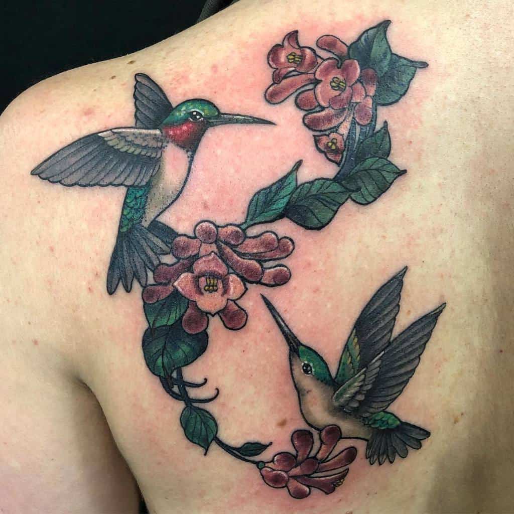 Bright and detailed back tattoo showcasing two hummingbirds feeding on honeysuckle blossoms