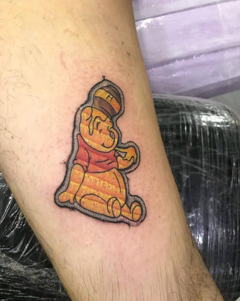 Tattoo of Winnie the Pooh sitting happily, created with a quilted embroidery look and thread-like shading.