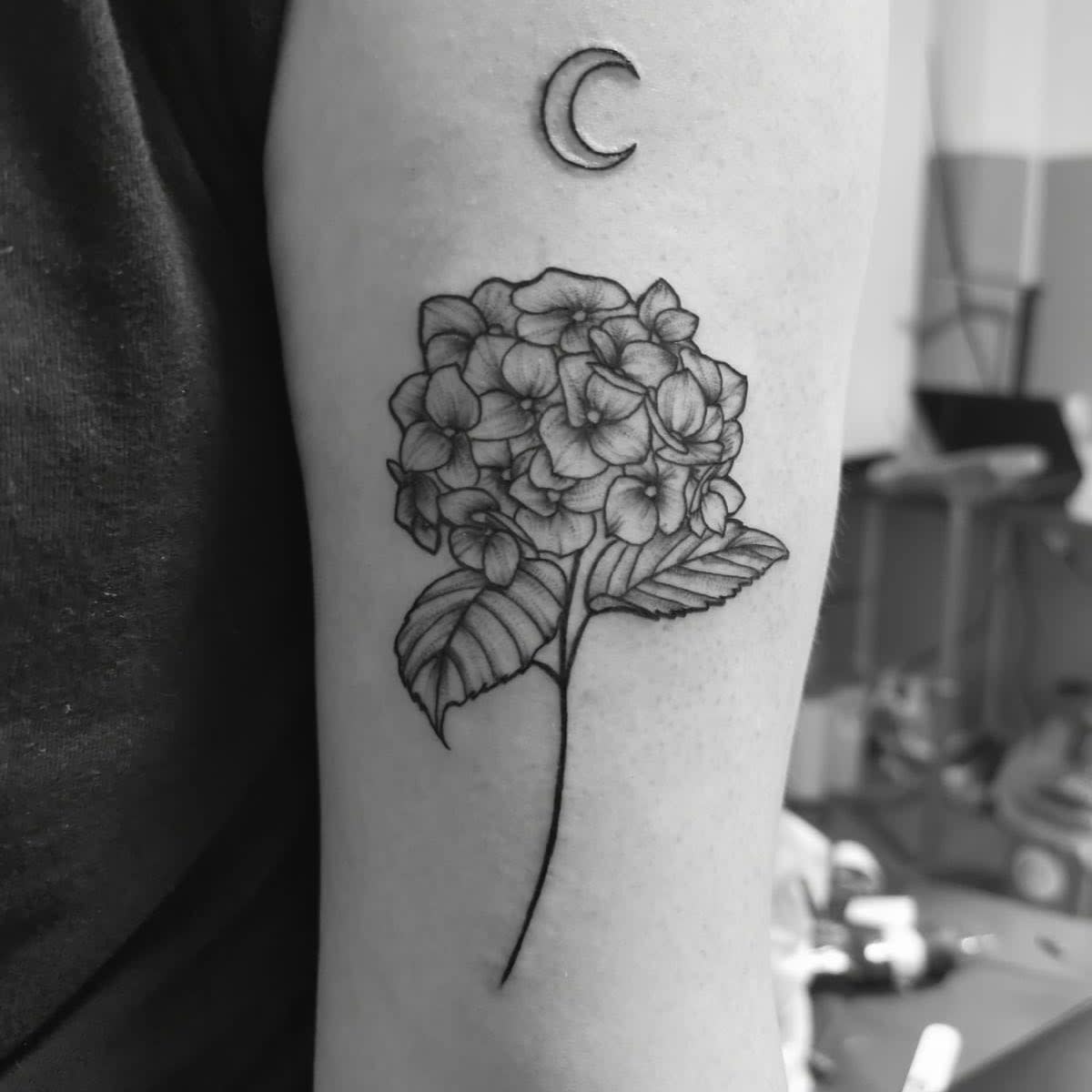 Black and white tattoo of hydrangea and a crescent moon on an arm