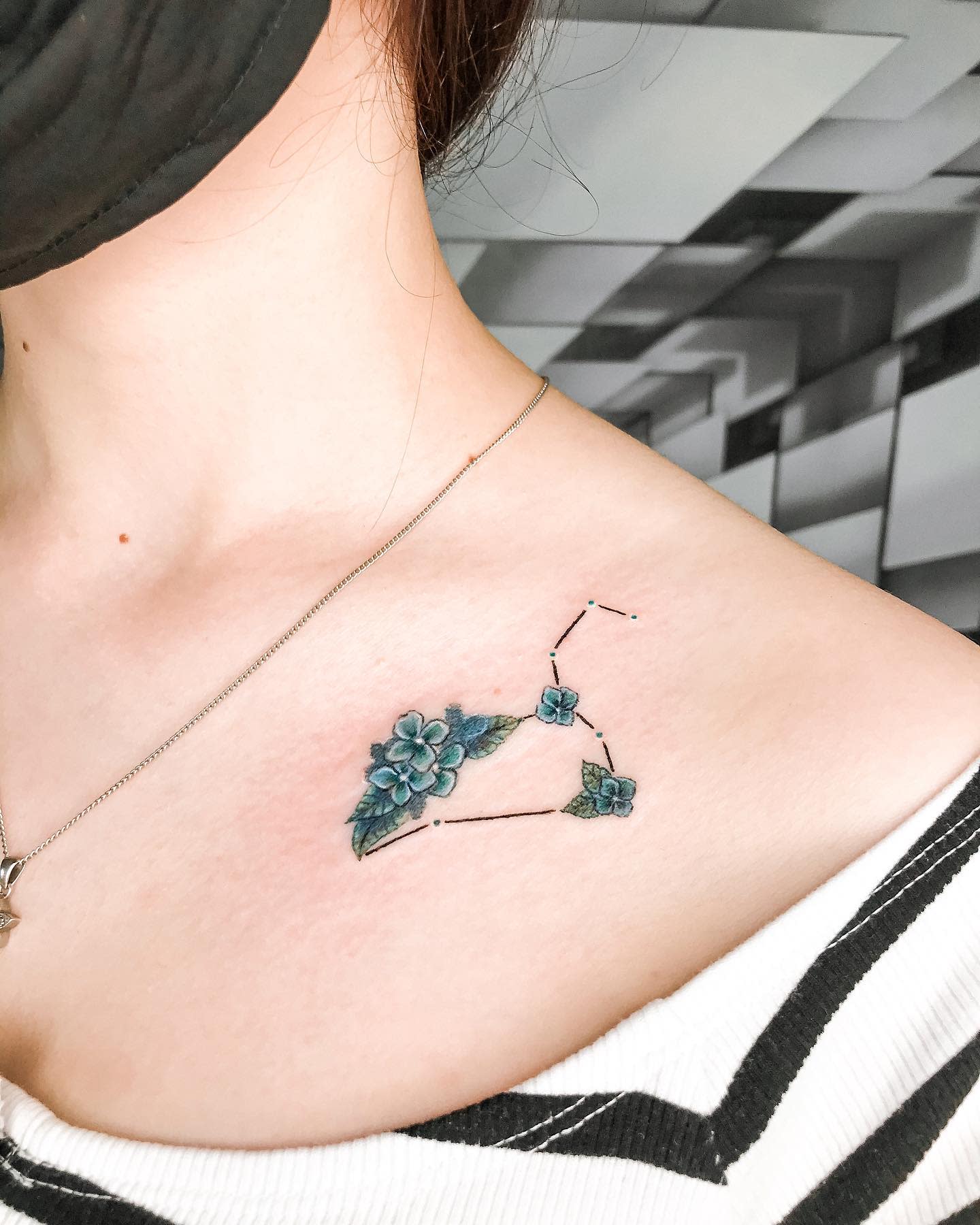A tattoo of the Libra constellation with blue flowers on the collarbone