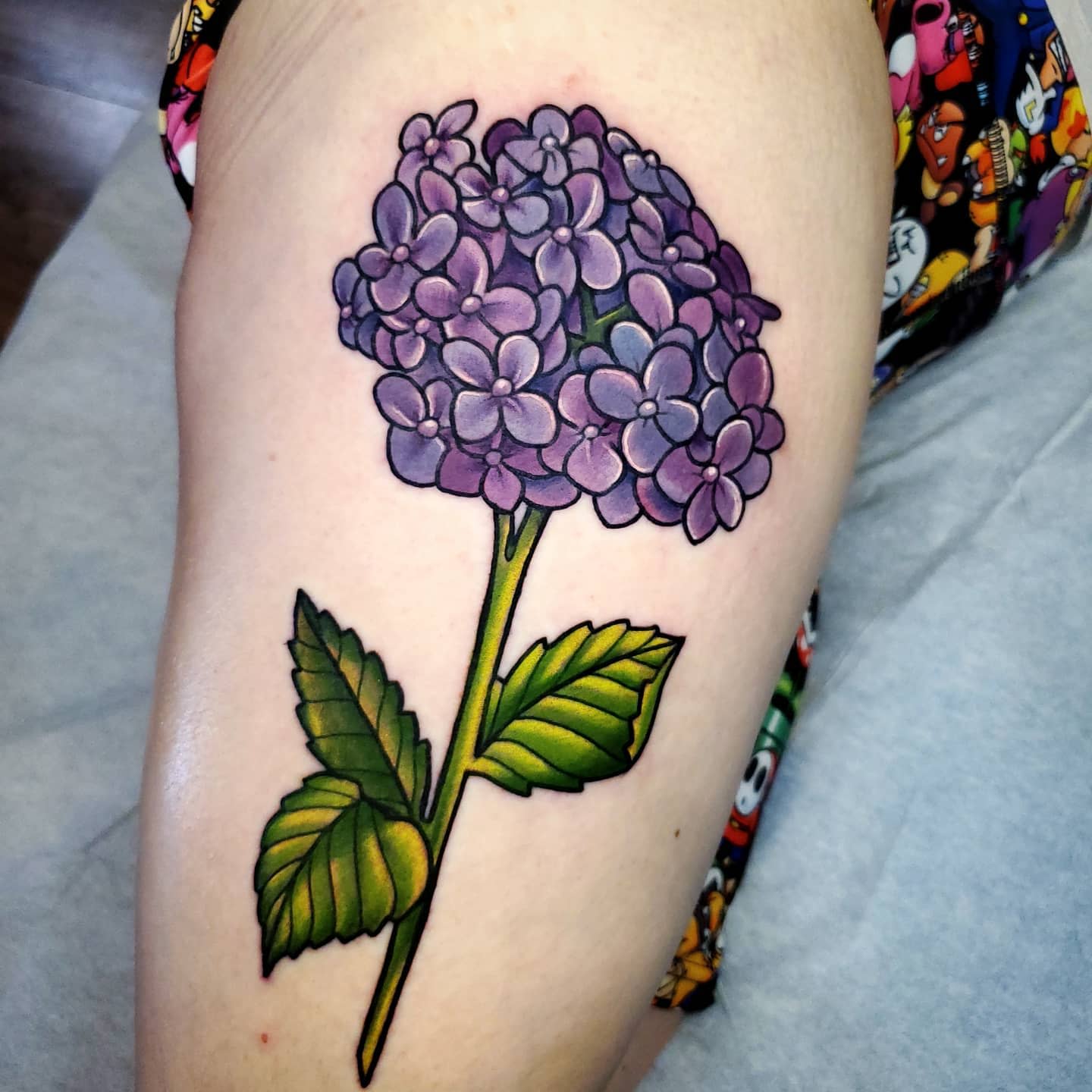 Tattoo of a purple hydrangea flower with green leaves on an upper arm
