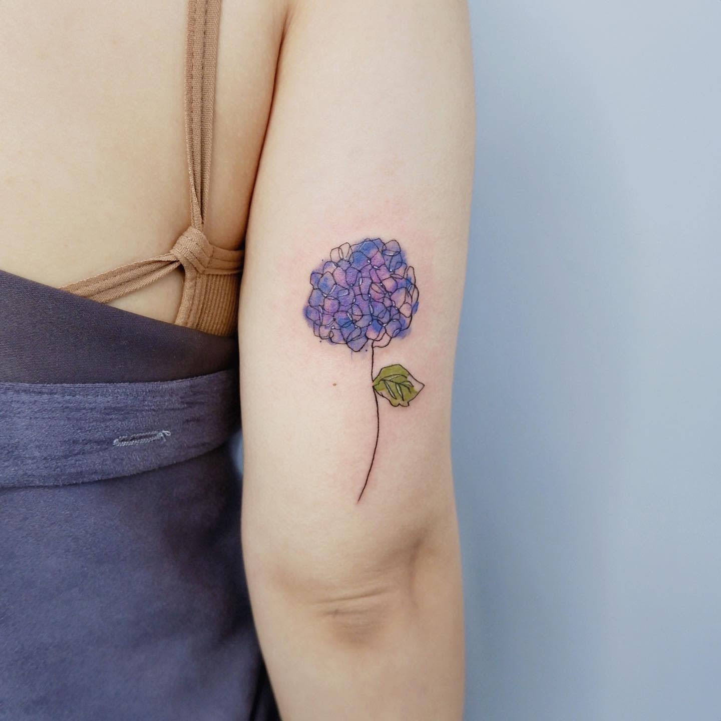 Purple hydrangea tattoo with a green leaf on an arm