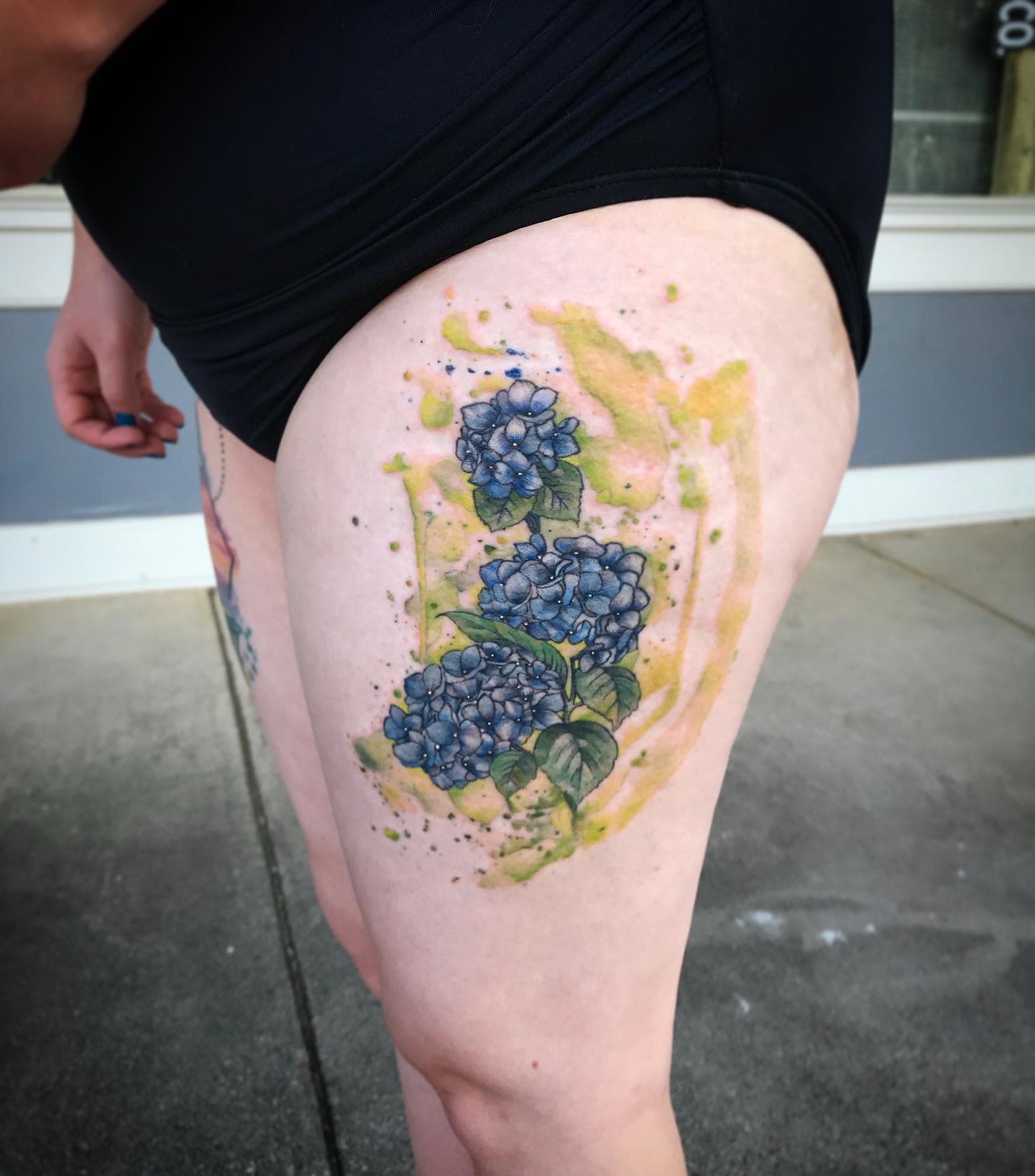 Thigh tattoo of purple flowers with green leaves