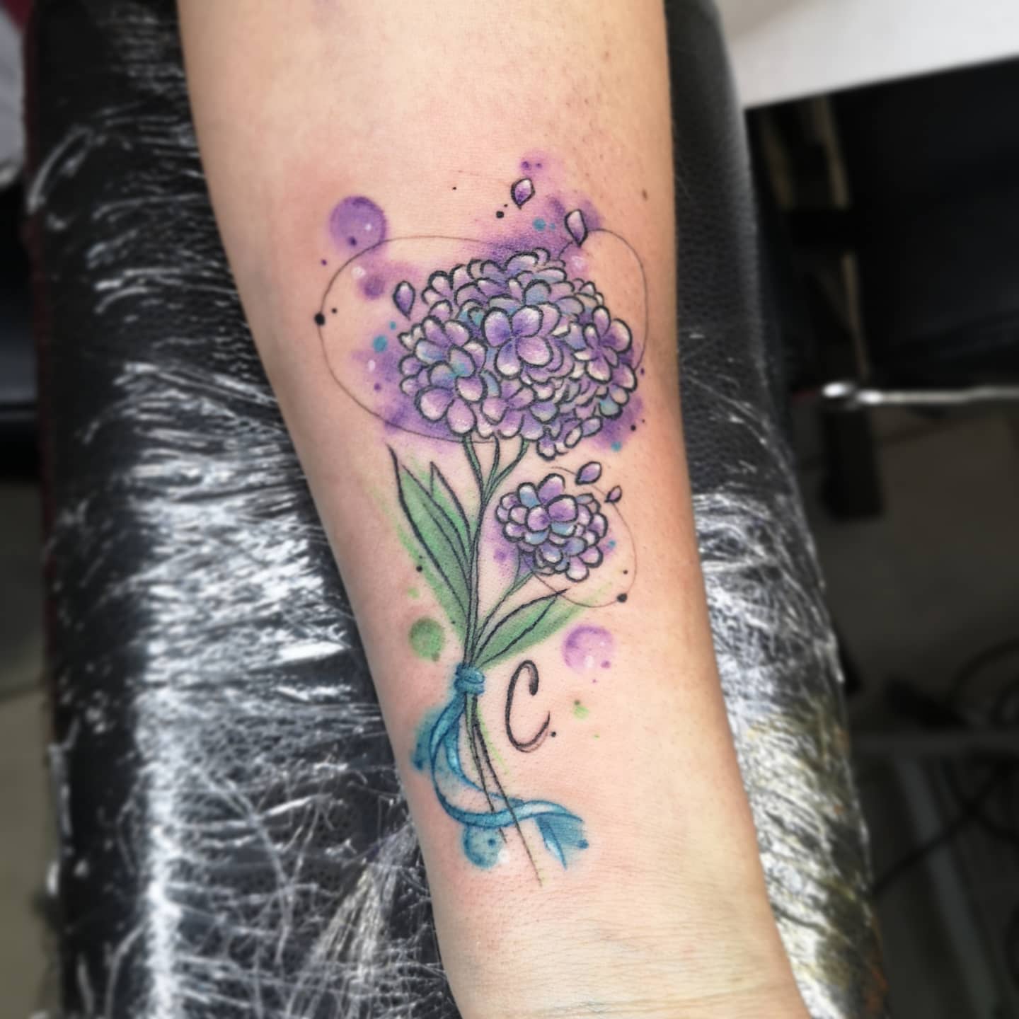 Forearm tattoo of two hydrangea flowers with leaves, featuring purple and green ink