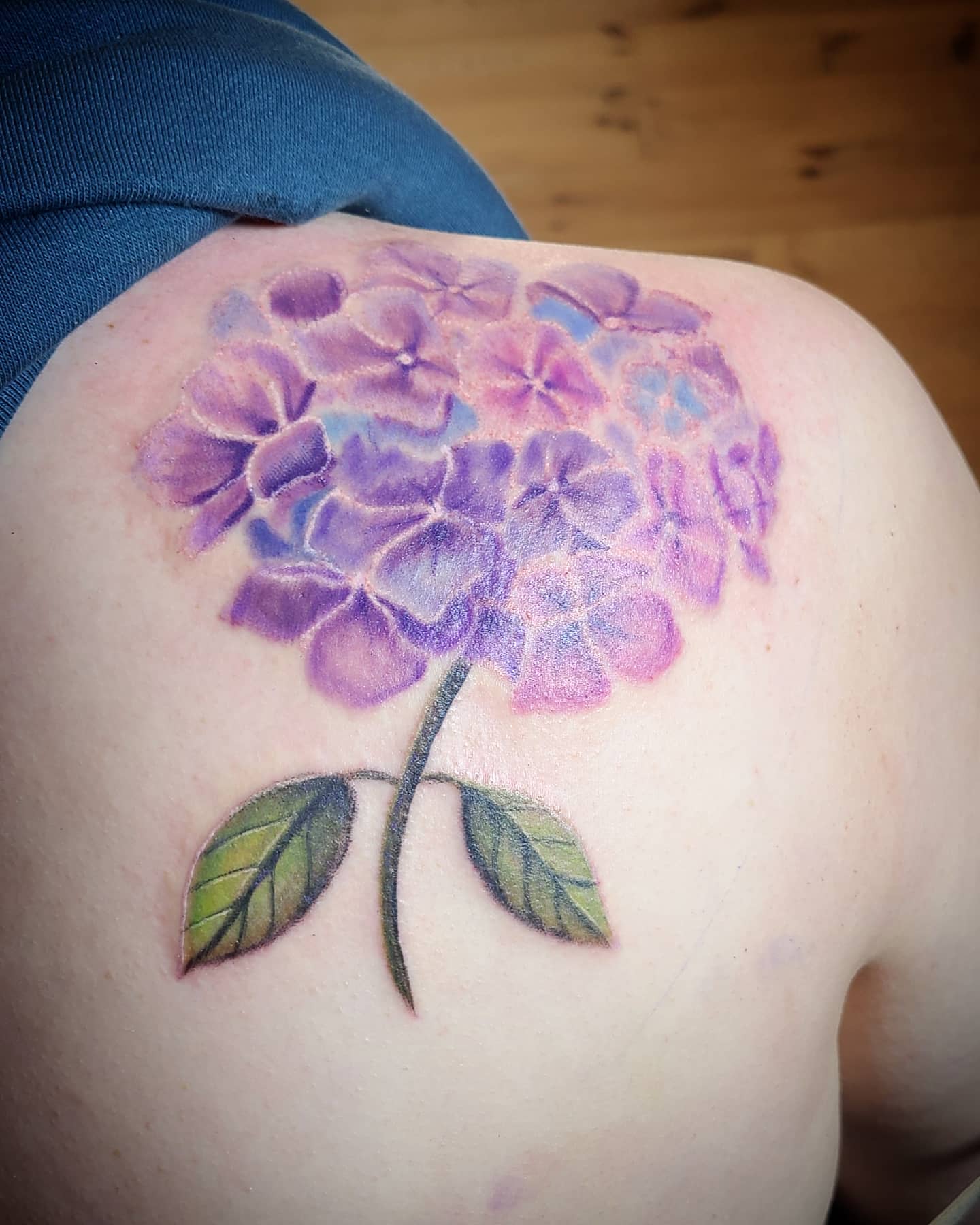 Tattoo of a purple hydrangea flower with green leaves on a shoulder
