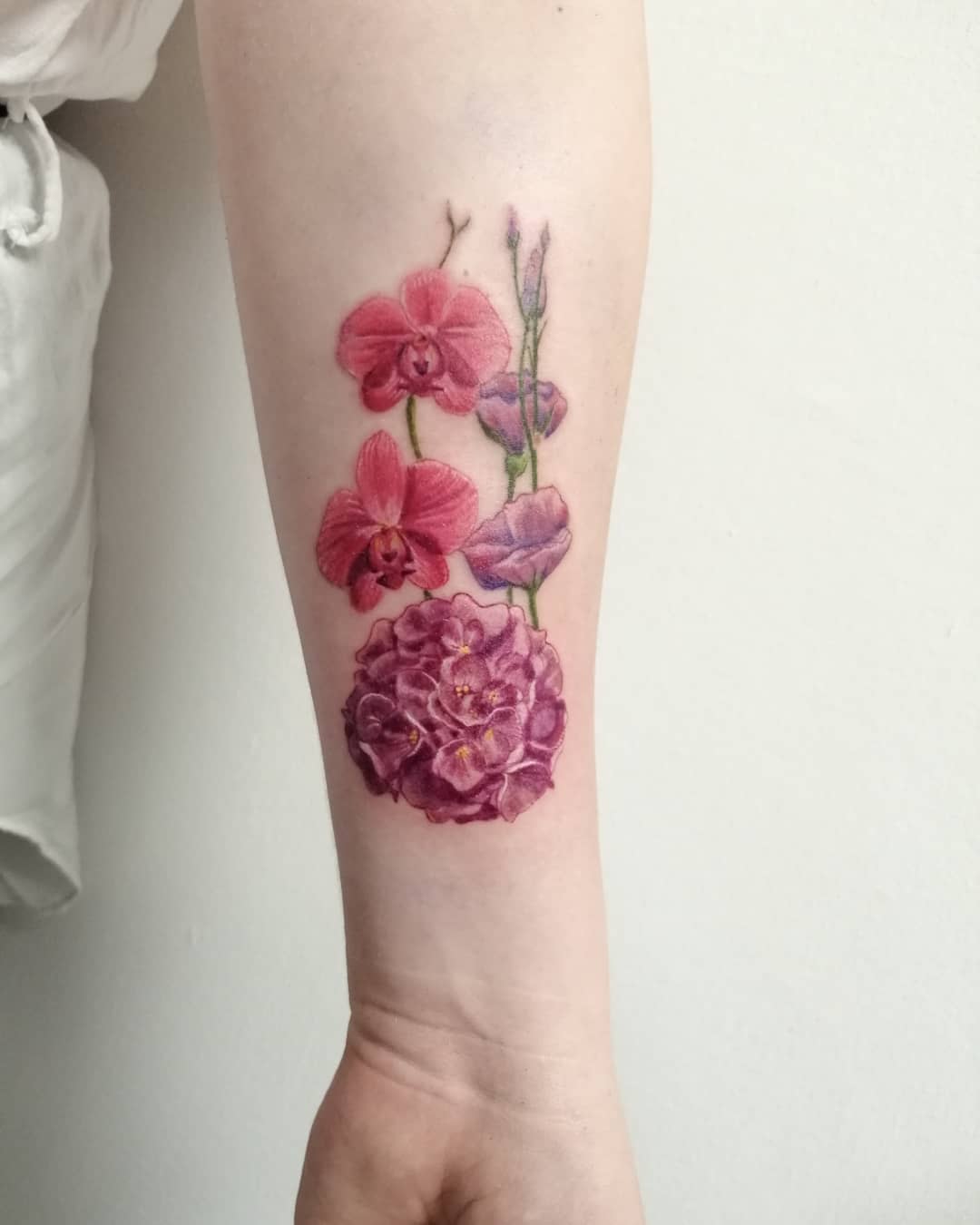 Tattoo of pink flowers on a wrist featuring orchids and a hydrangea