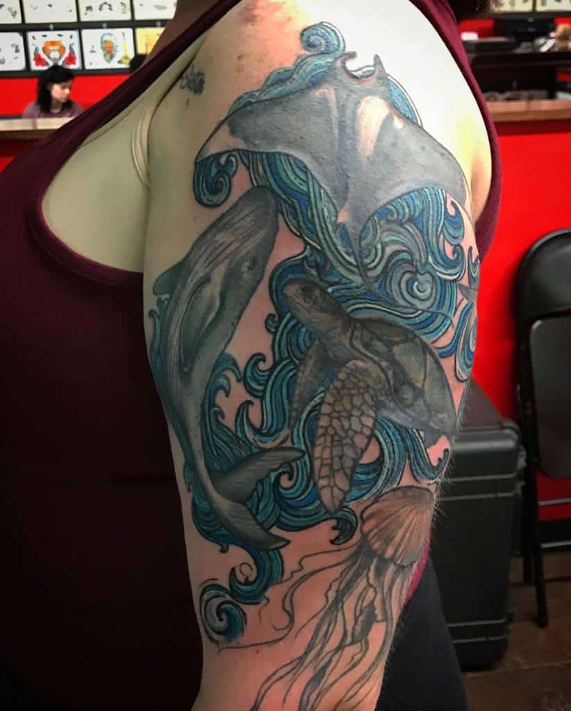Tattoo of ocean life including a manta ray, dolphins, sea turtle, and jellyfish