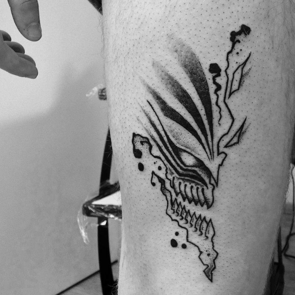 Black ink tattoo of Ichigo Kurosaki’s Hollow mask from Bleach, featuring sharp teeth, bold shading, and a fragmented design