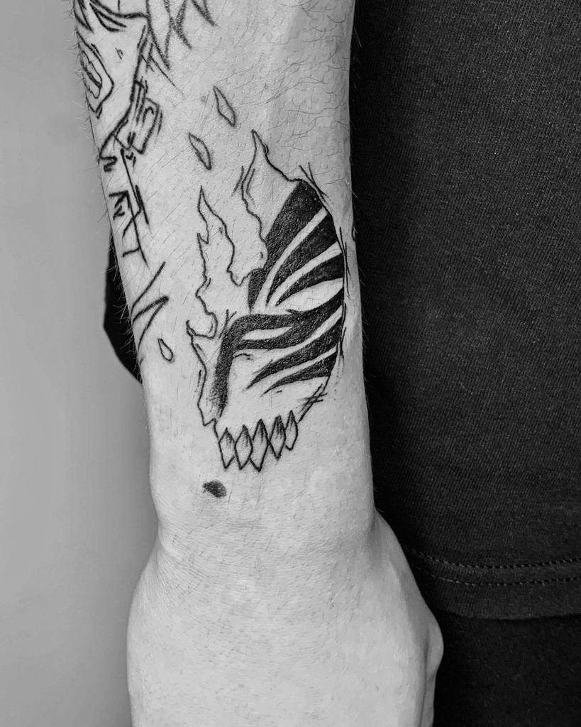 Black ink tattoo of Ichigo Kurosaki’s Hollow mask from Bleach, featuring a fragmented design with sharp teeth and bold linework