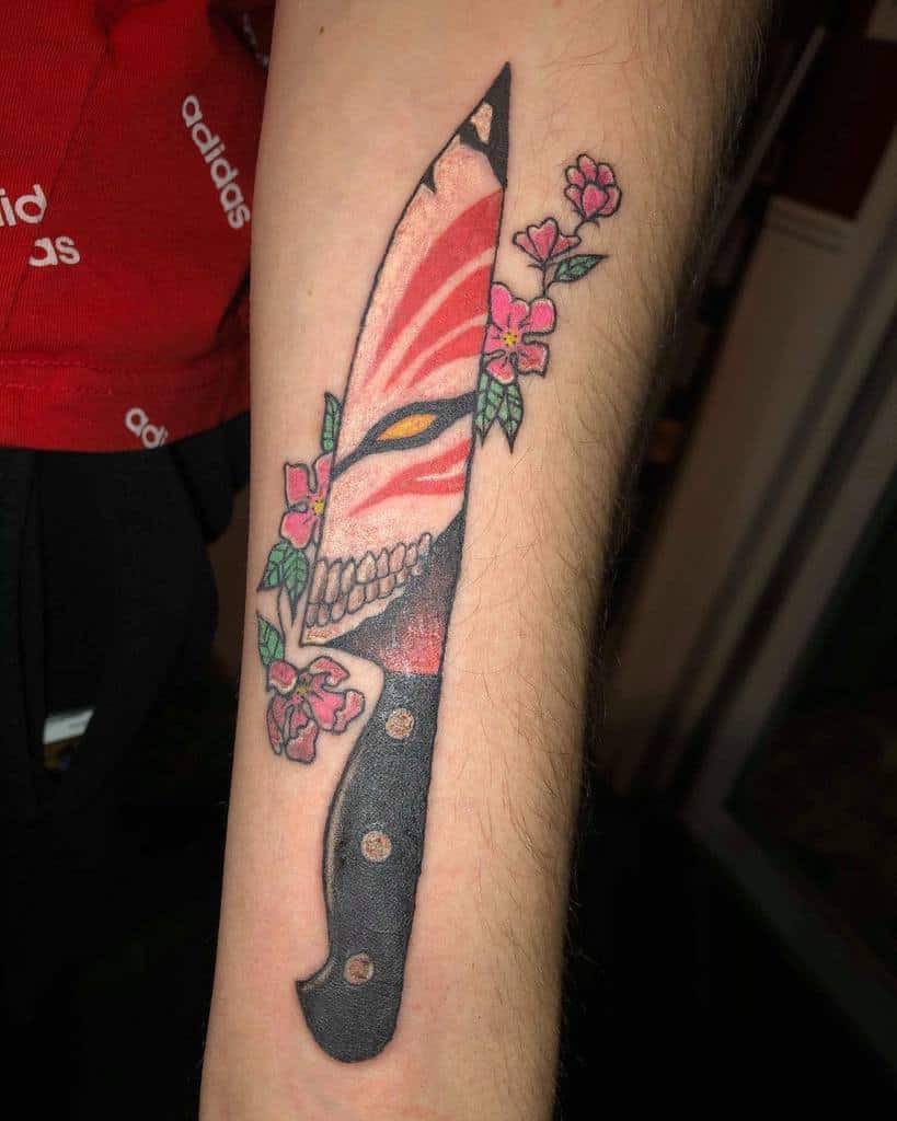 Creative tattoo of Ichigo Kurosaki’s Hollow mask from Bleach, integrated into a knife design with red and black shading, floral accents, and sharp details