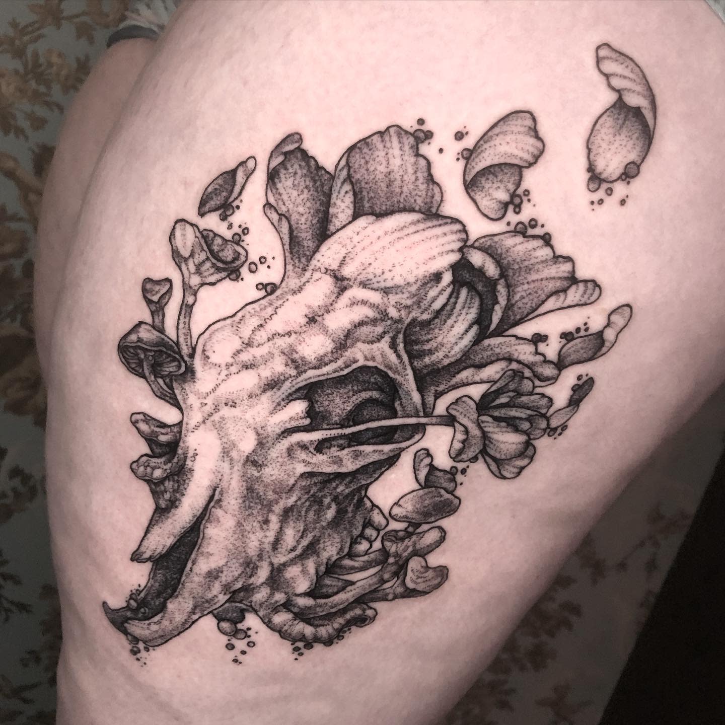 Black and white tattoo of a skull surrounded by abstract floral elements on an arm