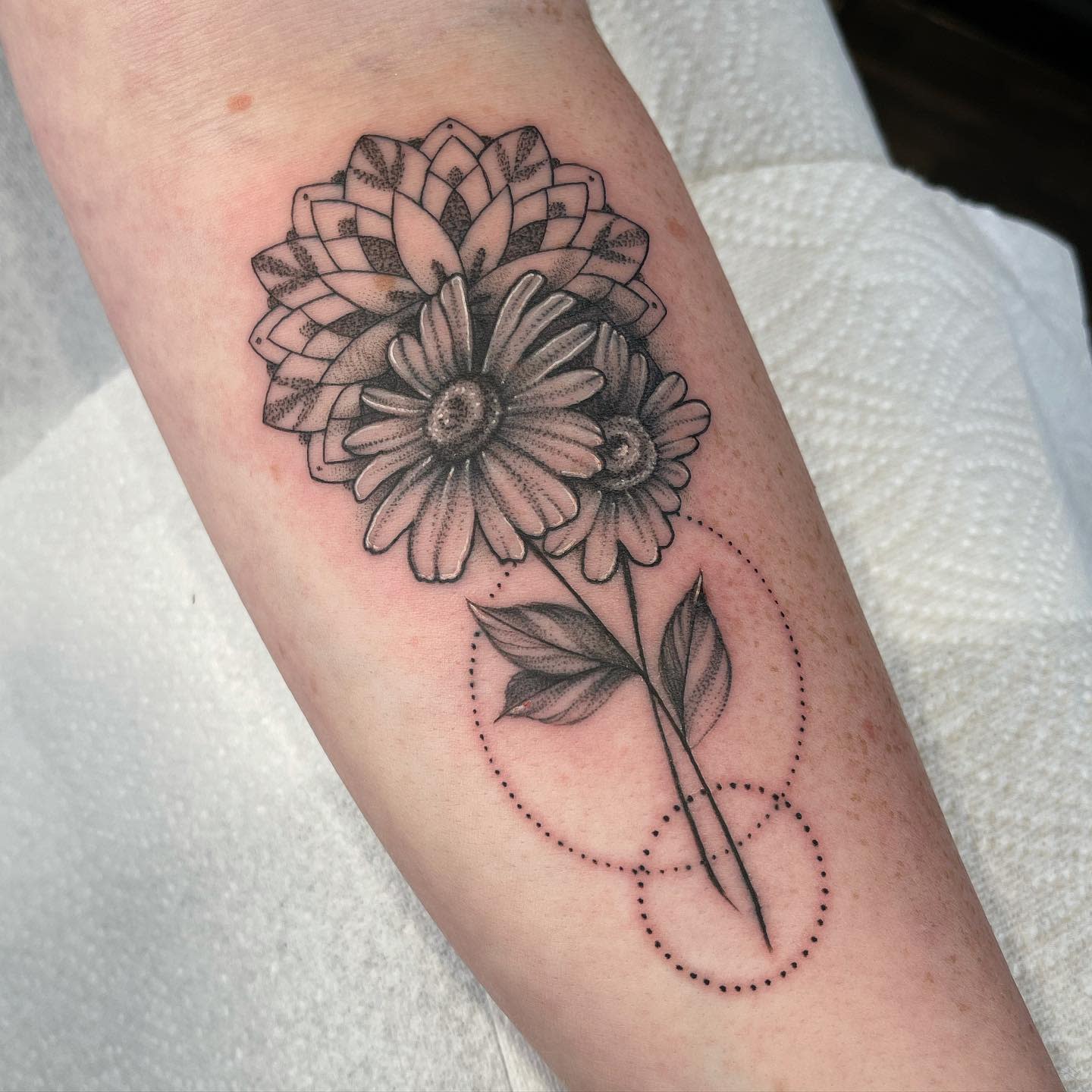 Black and gray floral tattoo with geometric elements on an inner forearm