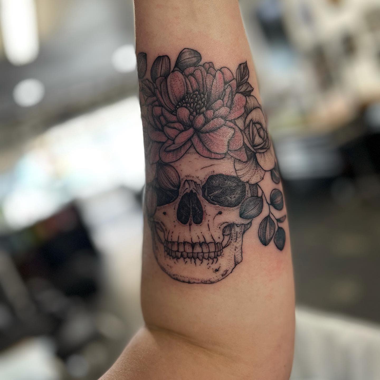 Tattoo of a skull with flowers on an inner forearm