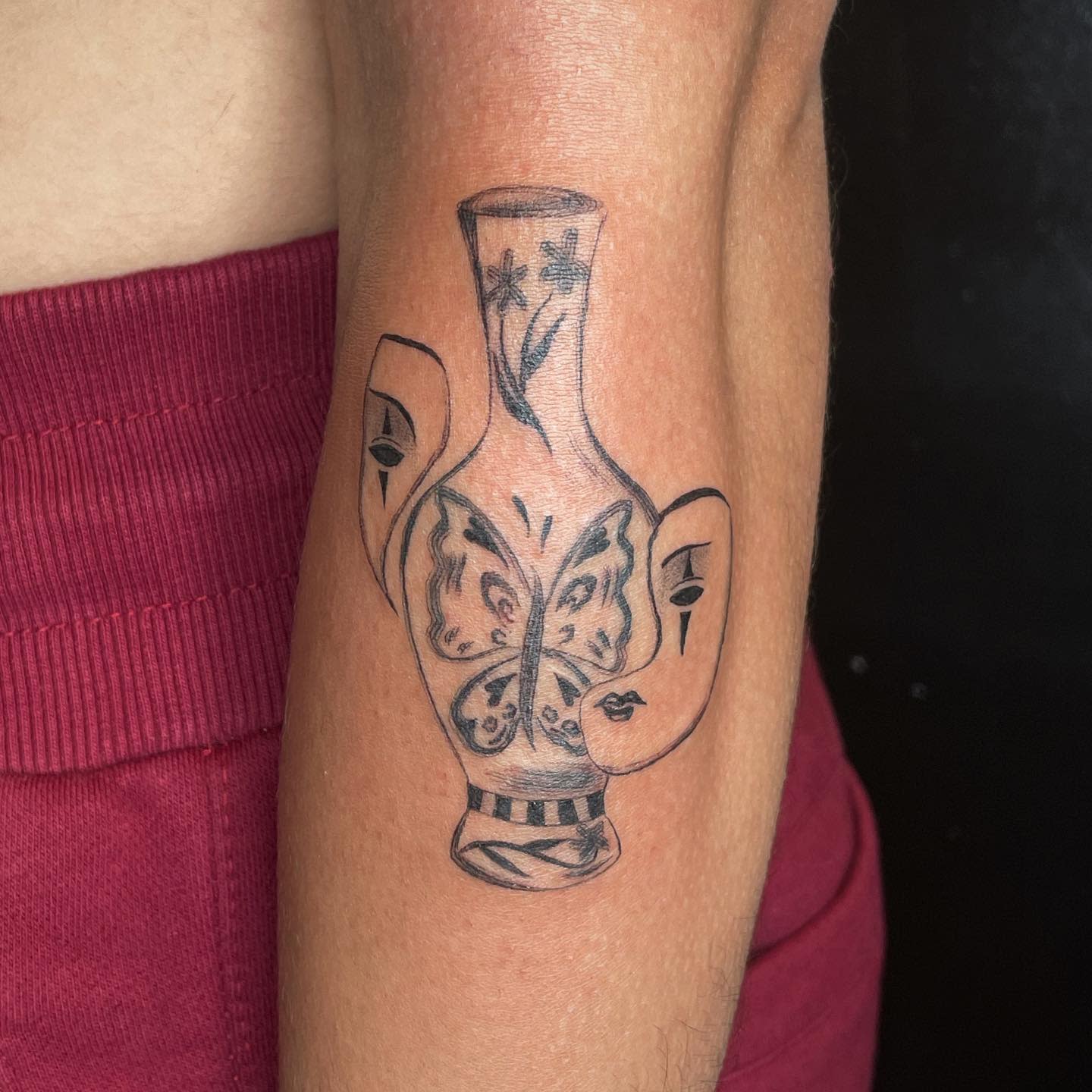 Arm tattoo featuring vase with butterfly and face designs on the inner forearm