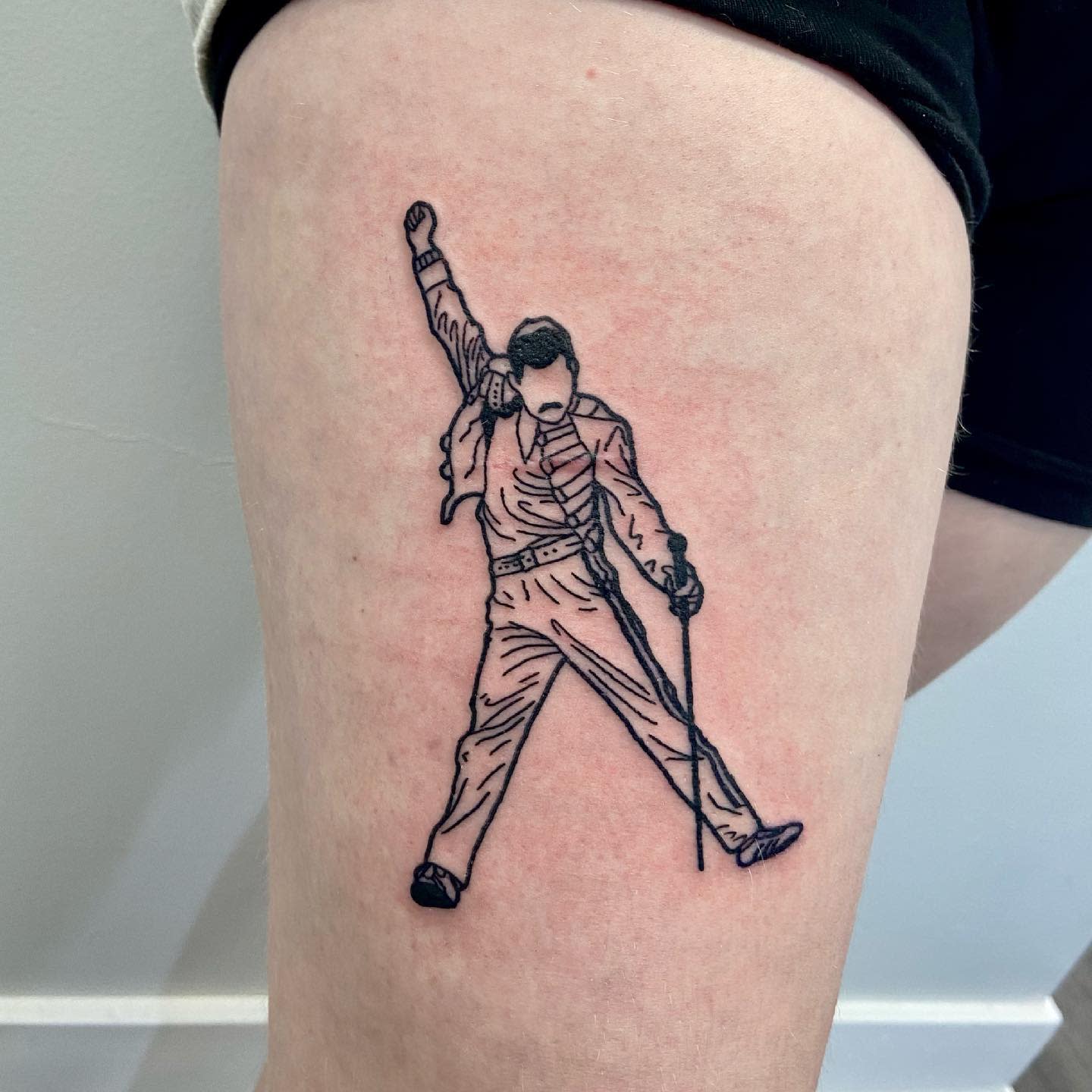 Tattoo of a Freddie Mercury with one arm raised holding a microphone stand