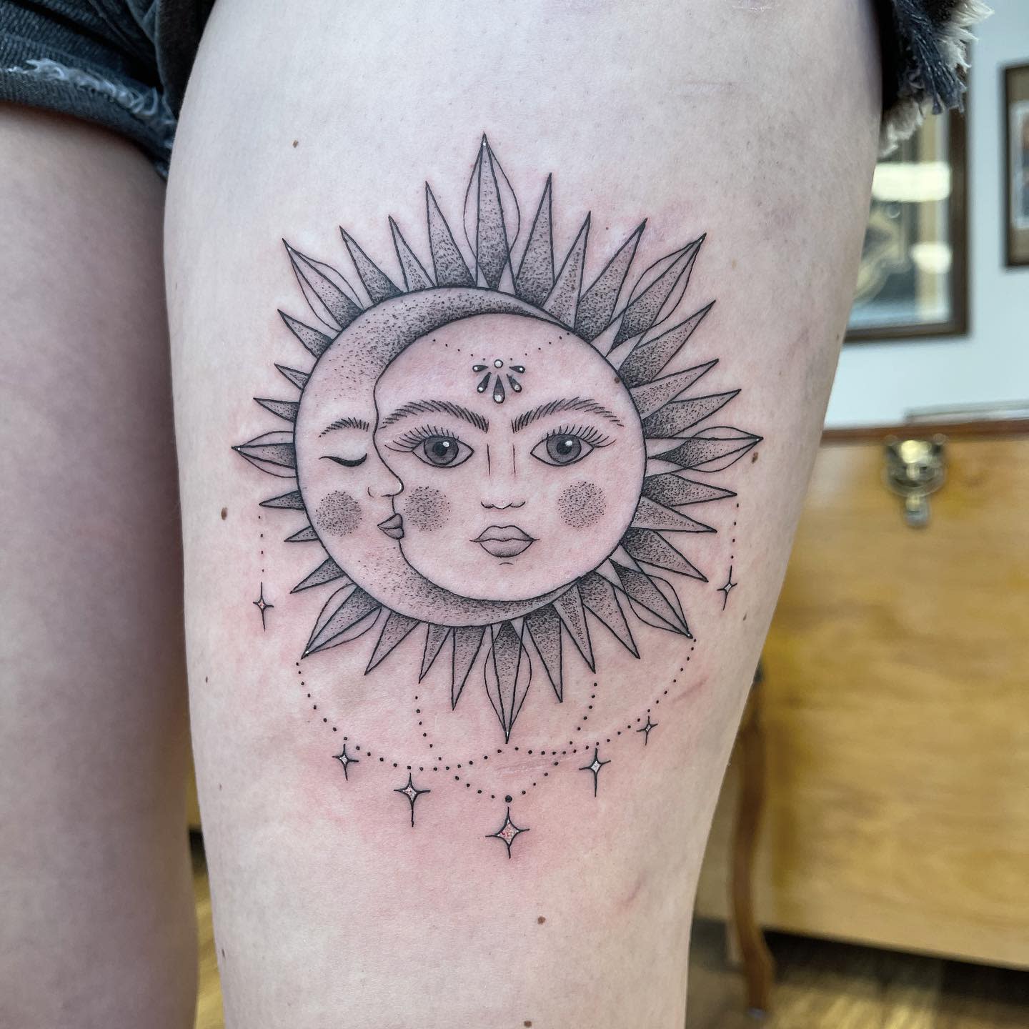Tattoo of a sun and moon with faces, and stars on a thigh