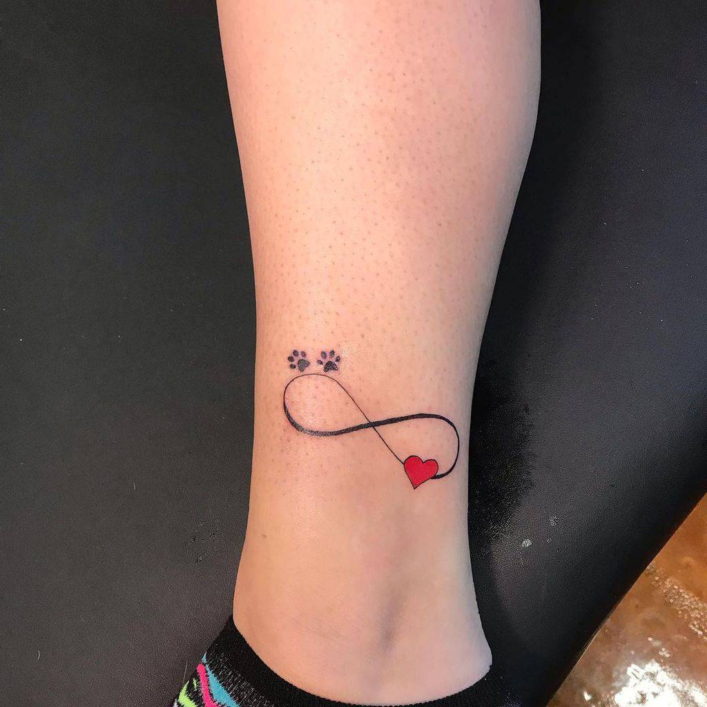 Tattoo of an infinity loop with a paw print on one end and a red heart on the other on a leg, symbolizing endless love
