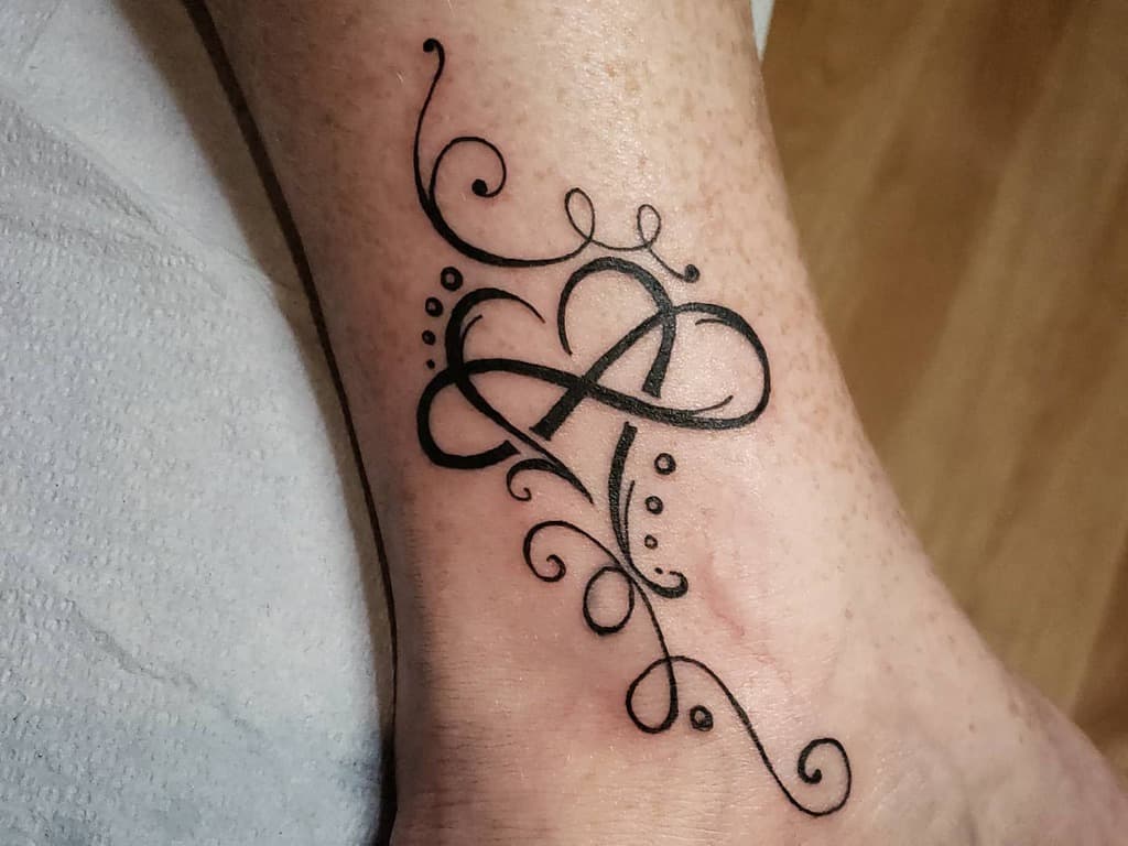 Tattoo featuring an elegant black infinity symbol intertwined with a heart, adorned with decorative swirls