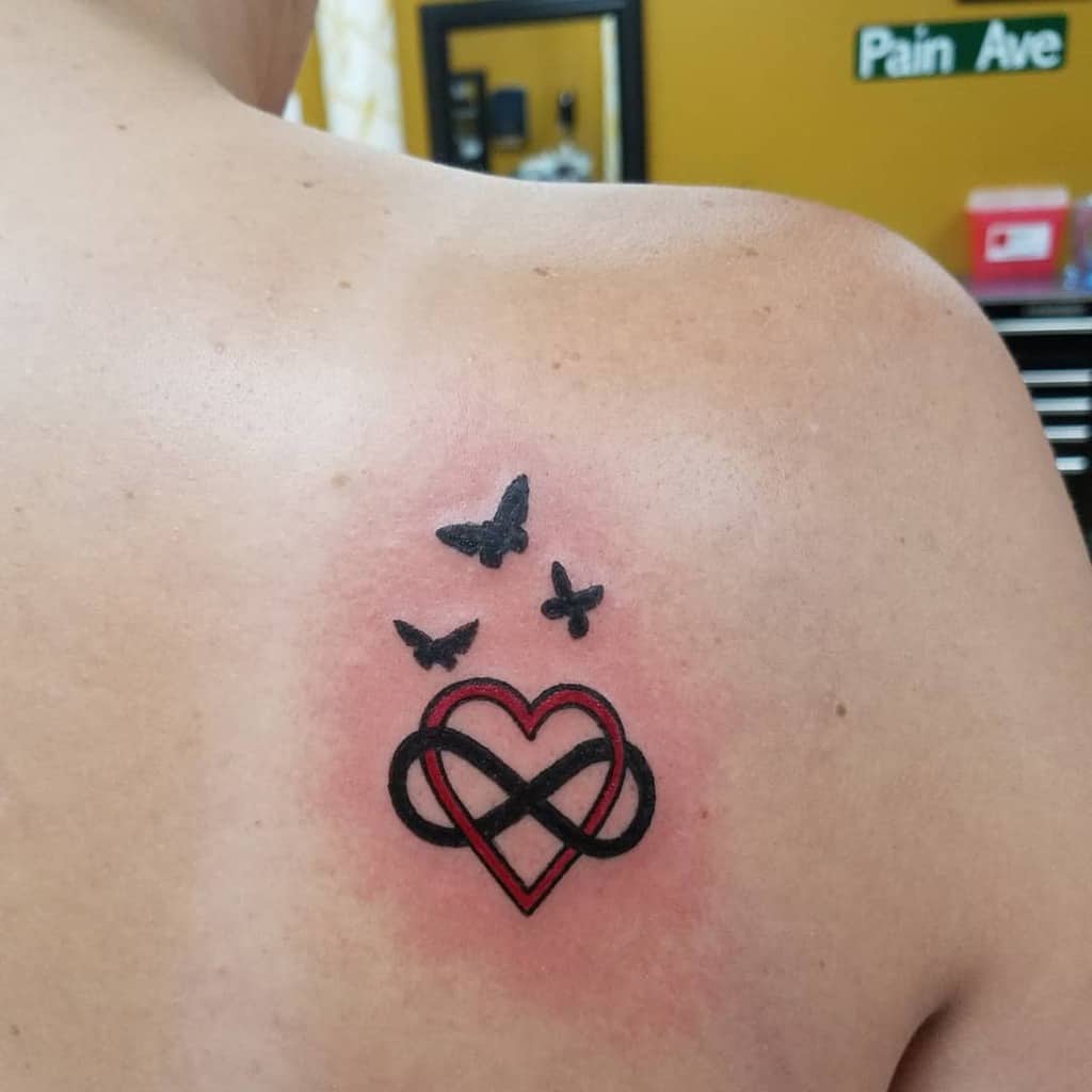 Tattoo on a person's back featuring a heart intertwined with an infinity symbol, and three small birds above it