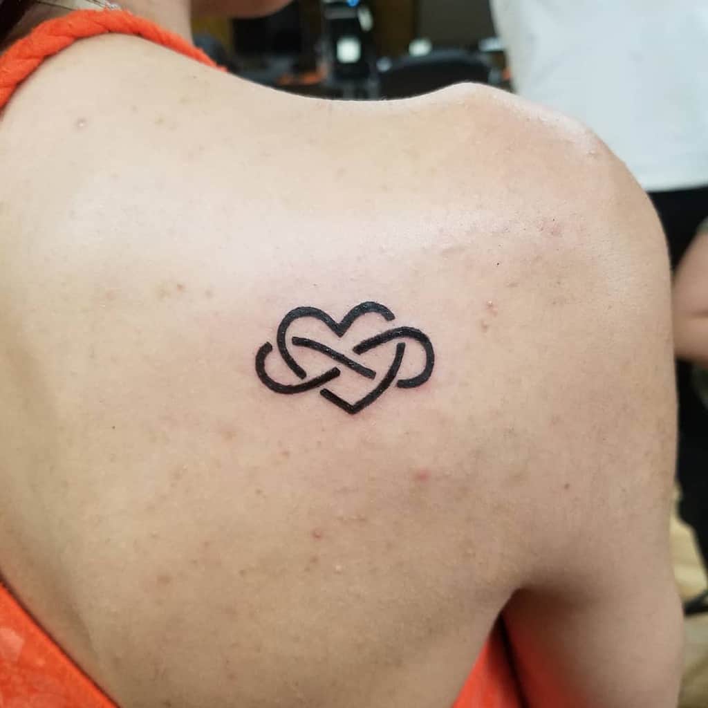 An elegant infinity heart tattoo graces the woman's upper back