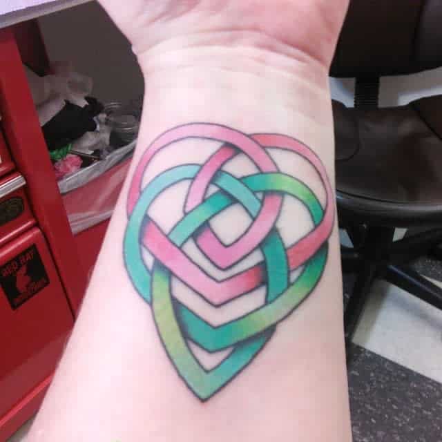 Colorful interwoven heart tattoo on a wrist, featuring pink, blue, and green strands that beautifully form an infinity symbol
