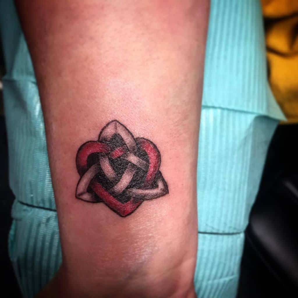 Tattoo of an intricate, entwined heart design with elements of infinity in black and red ink on a forearm