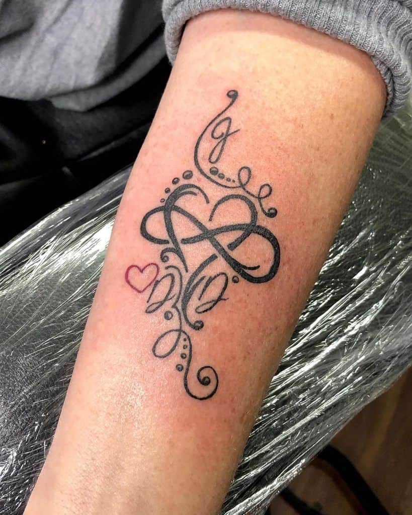 Forearm tattoo featuring an infinity symbol with decorative swirls, dots, and a small red heart