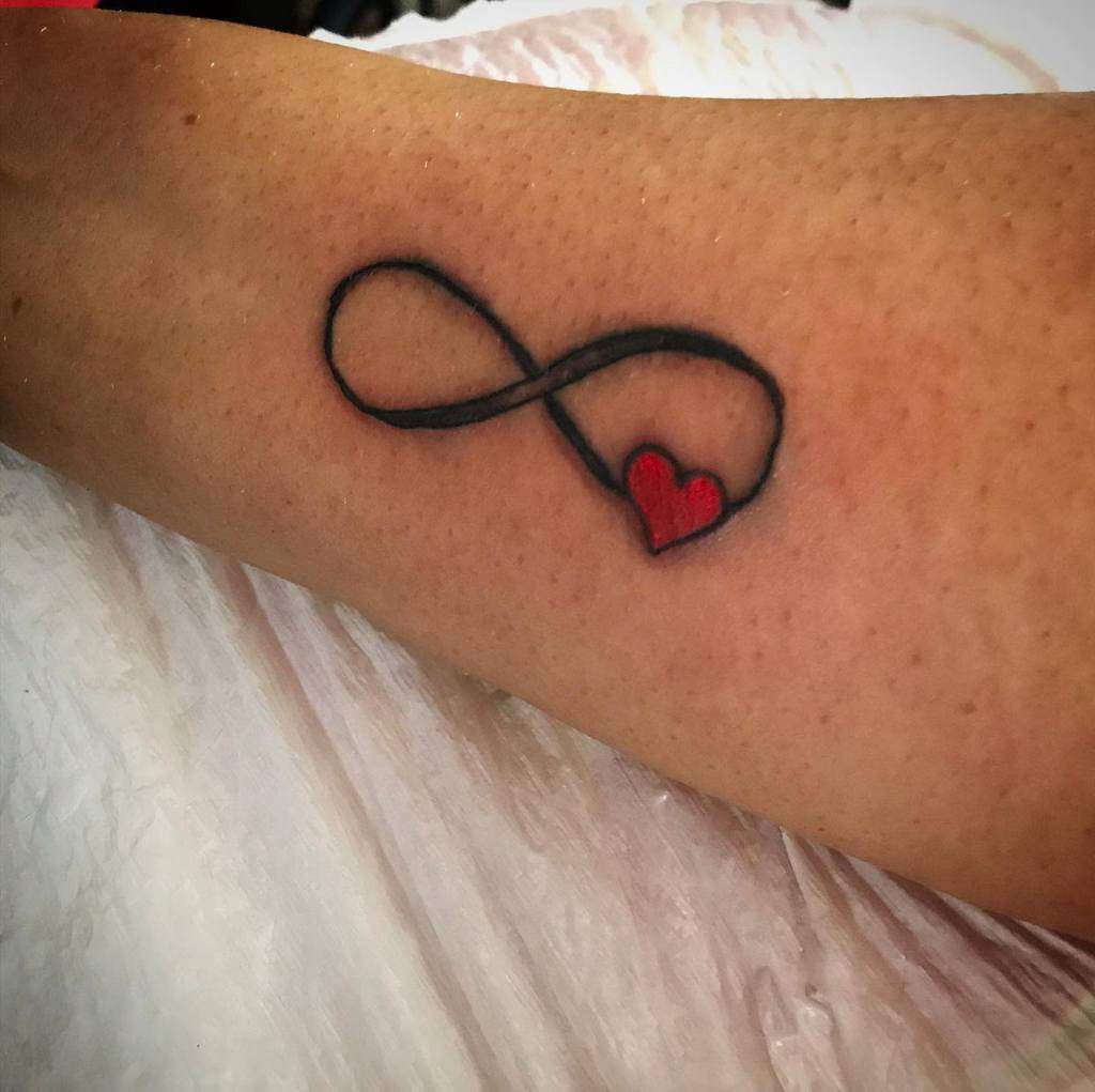 Infinity symbol tattoo with a red heart delicately placed at the end on an arm