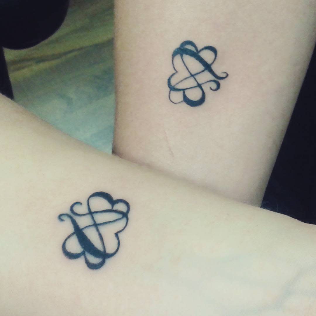 Two arms with matching abstract black infinity tattoos in a symmetrical design