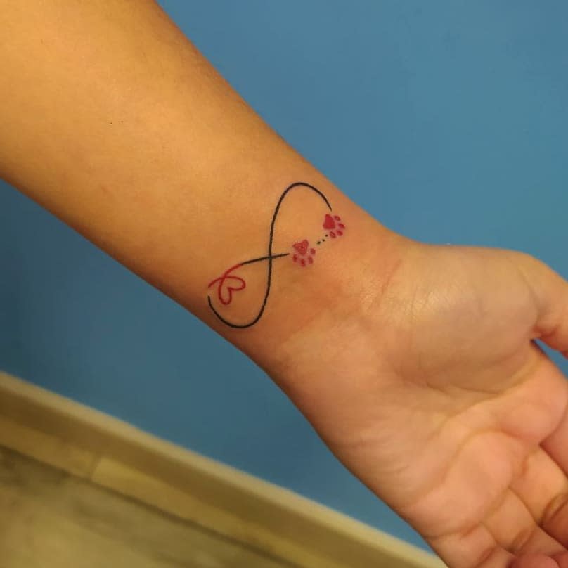 An infinity symbol intertwined with paw prints and a delicate heart tattooed on a wrist