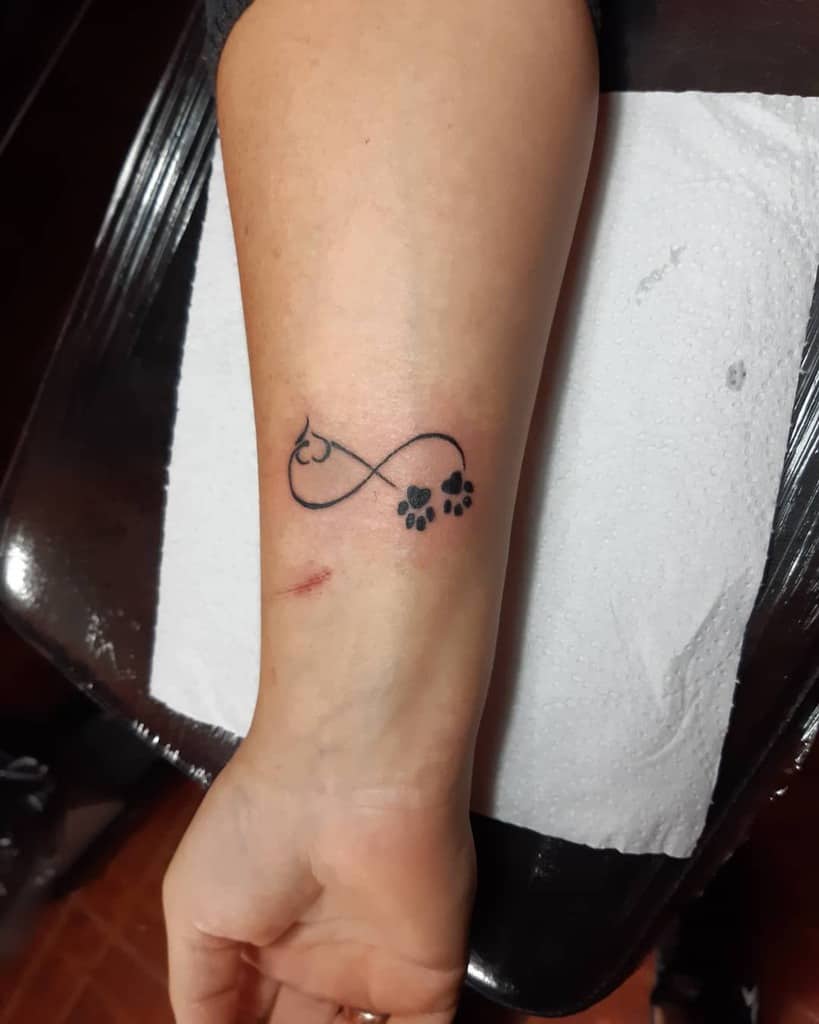 Infinity tattoo with a heart-shaped cat outline and paw prints on a forearm