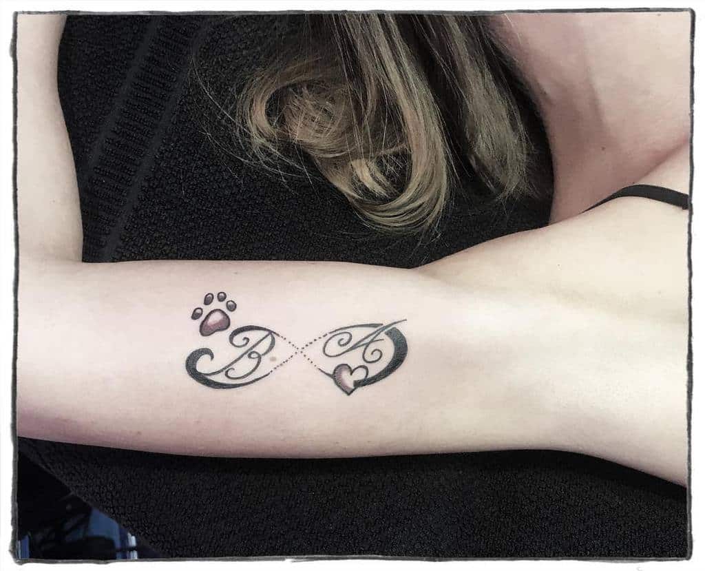 Tattoo of hearts, paw prints, and initials "B" and "A" seamlessly forming an infinity symbol on a forearm