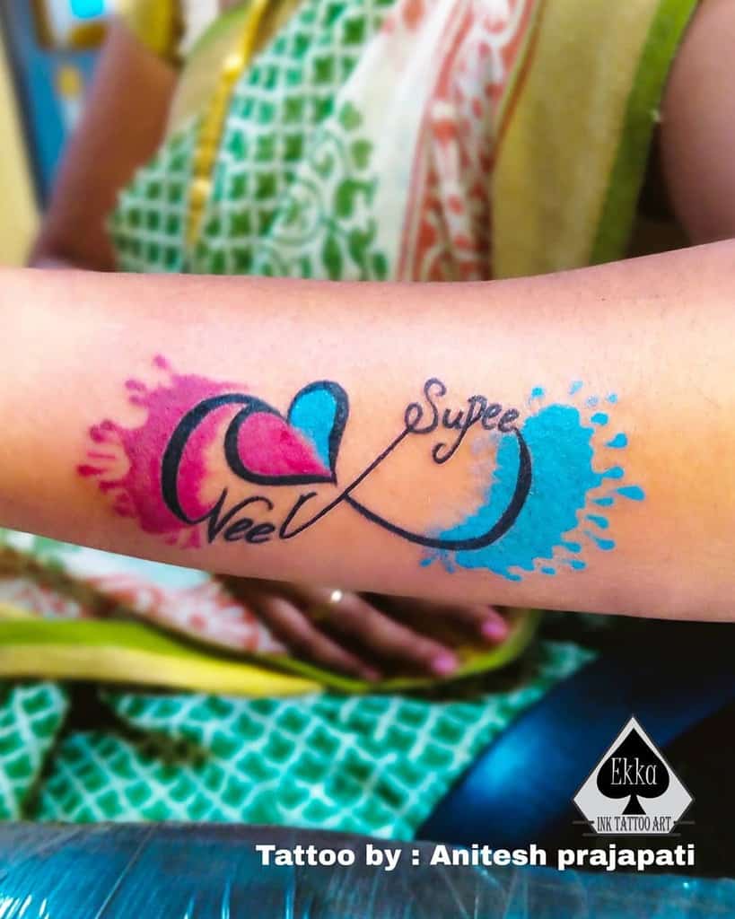 An infinity symbol tattoo with intertwined hearts and vibrant splashes of color graces a forearm