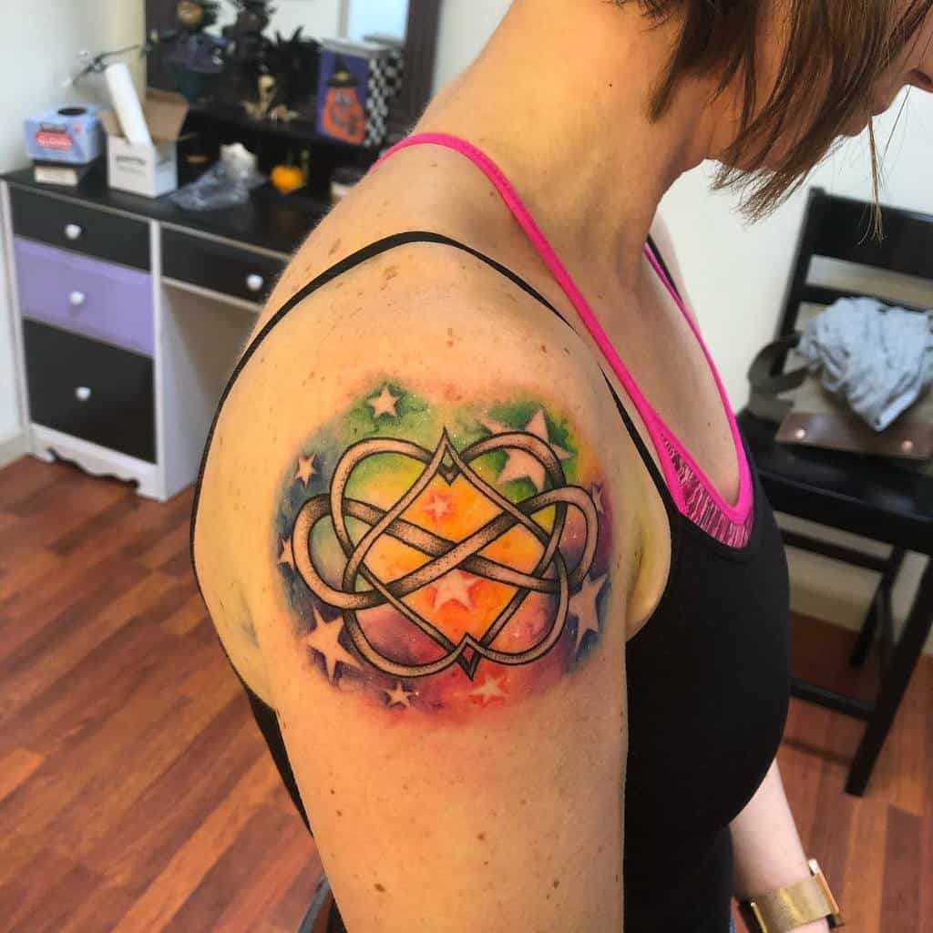 Woman showcasing a colorful geometric infinity tattoo on her upper arm, stars twinkling in the background