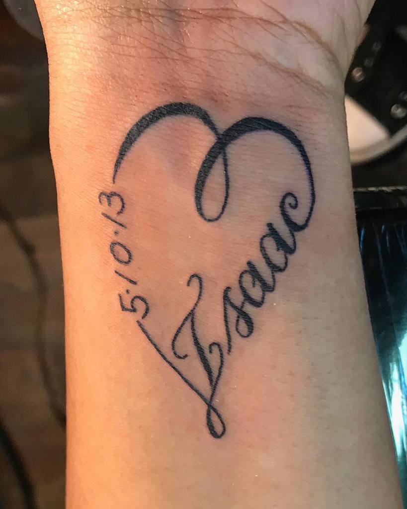Tattoo with the name "Isaac" inside a heart outline, and the date "5/10/13" on a wrist