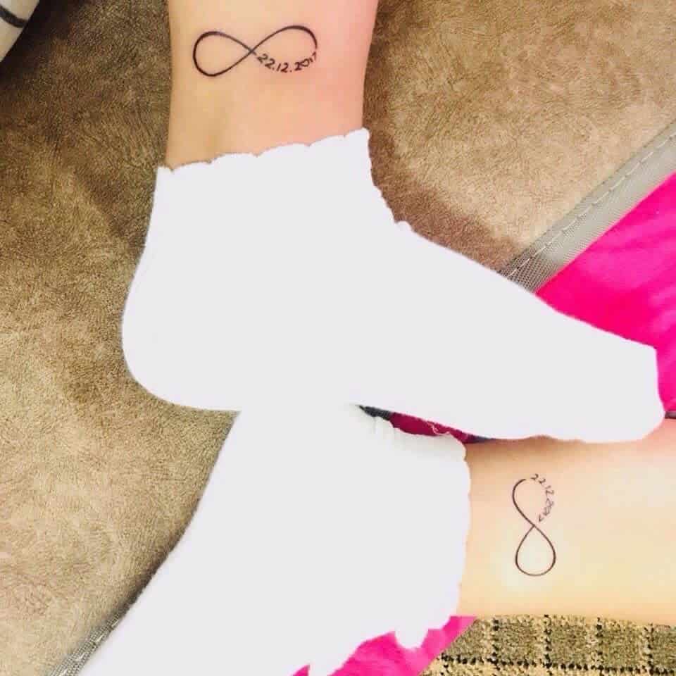 Matching infinity symbol tattoos with dates on two ankles
