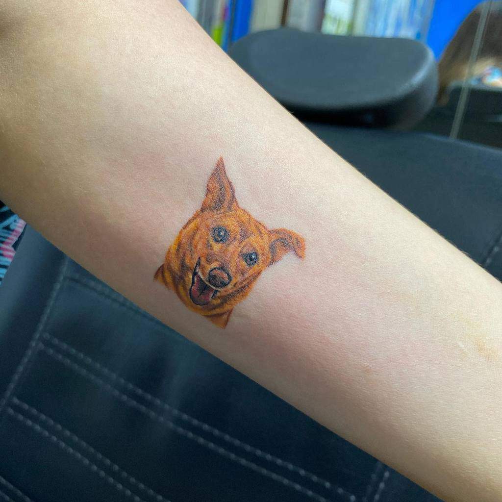 A small tattoo of a happy dog's face on a forearm
