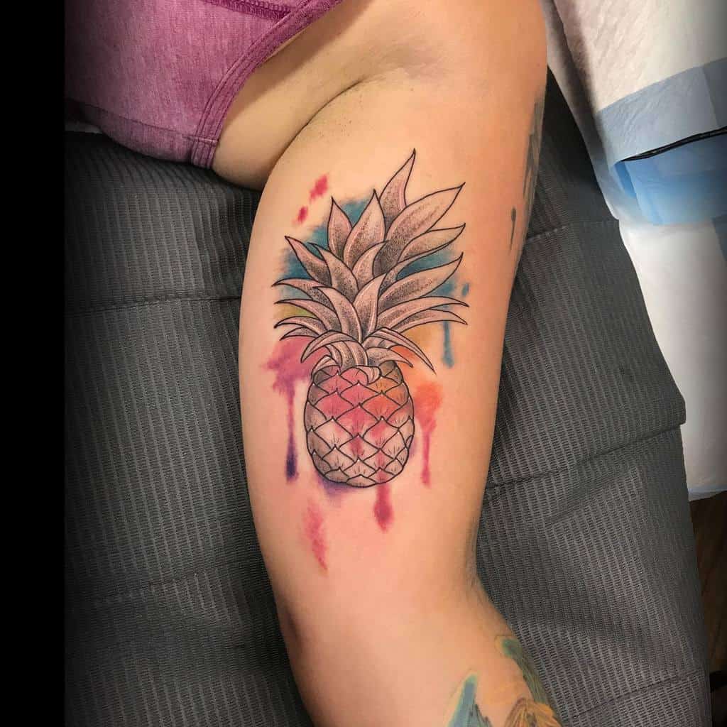 Tattoo of a pineapple with watercolor splashes on an arm
