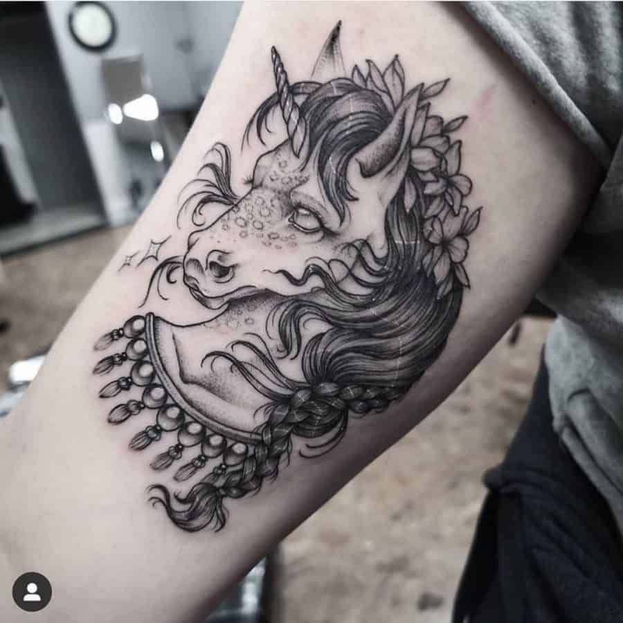 Detailed black ink tattoo of a unicorn with a braided mane, floral crown, and ornate jewelry, blending fantasy with bohemian elegance.